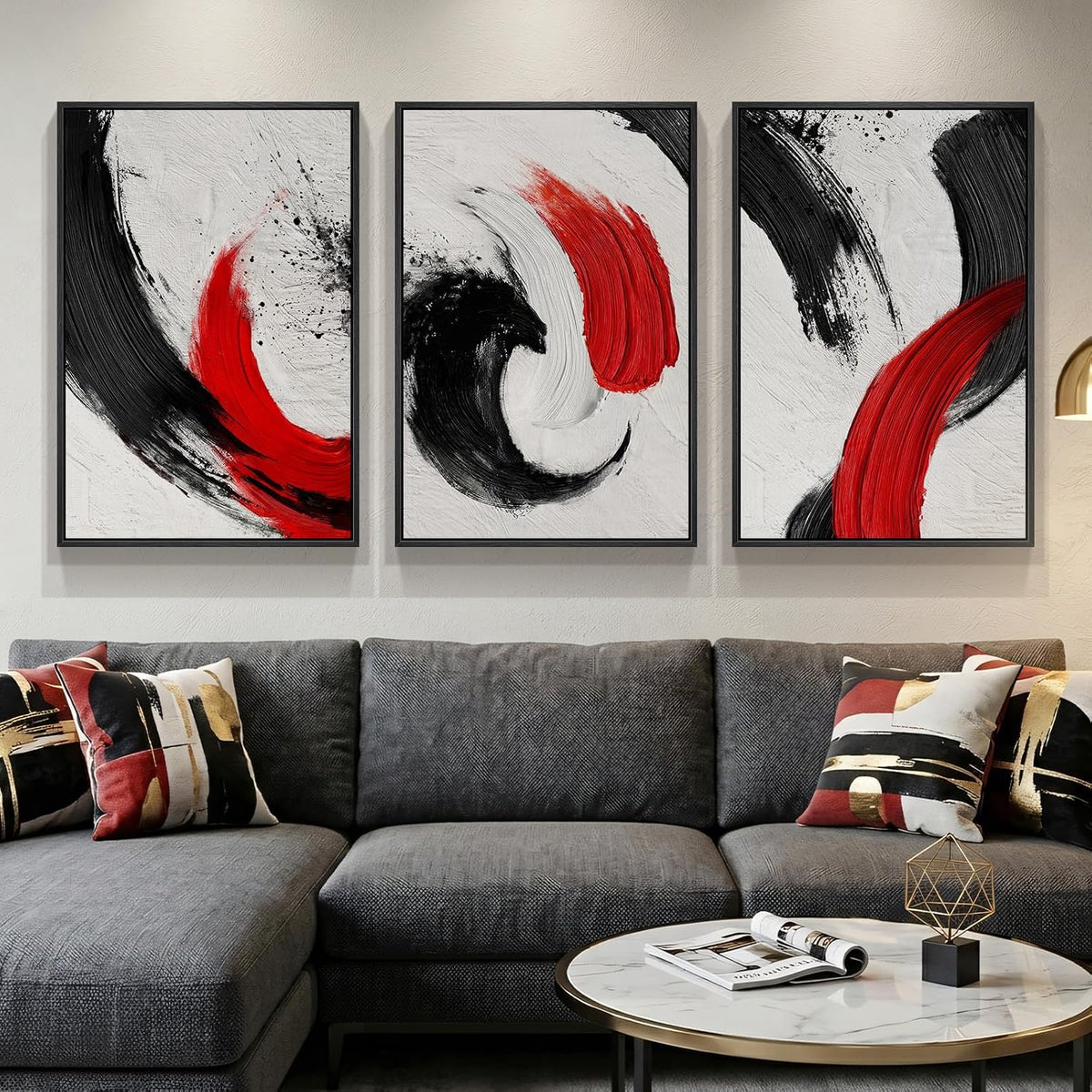 Three framed panels with bold red and black brushstrokes hung above a charcoal sofa with patterned throw pillows and a round