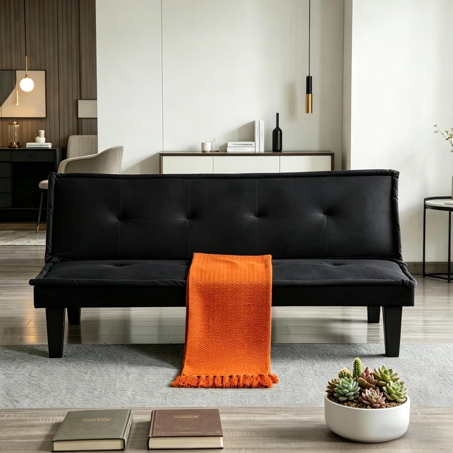 Front view of a black velvet futon sofa with an orange throw draped over the seat and a small succulent bowl on the floor.