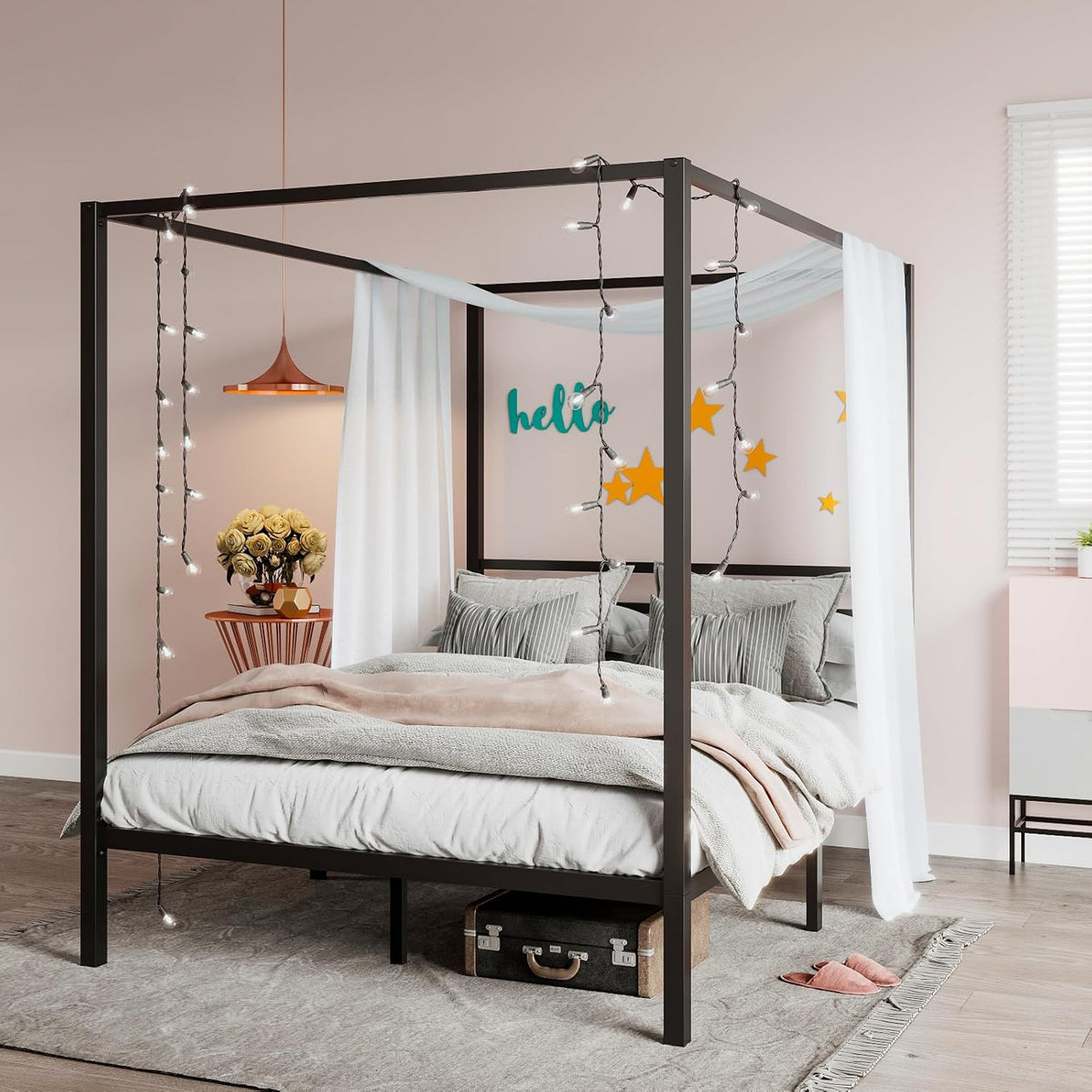 Black metal four-poster canopy bed staged with sheer curtains, hanging string lights, pillows and a blanket.