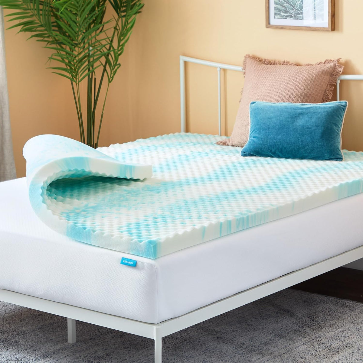 Close-up of an egg‑crate textured teal-and-white foam topper curled at the corner on a white platform bed.
