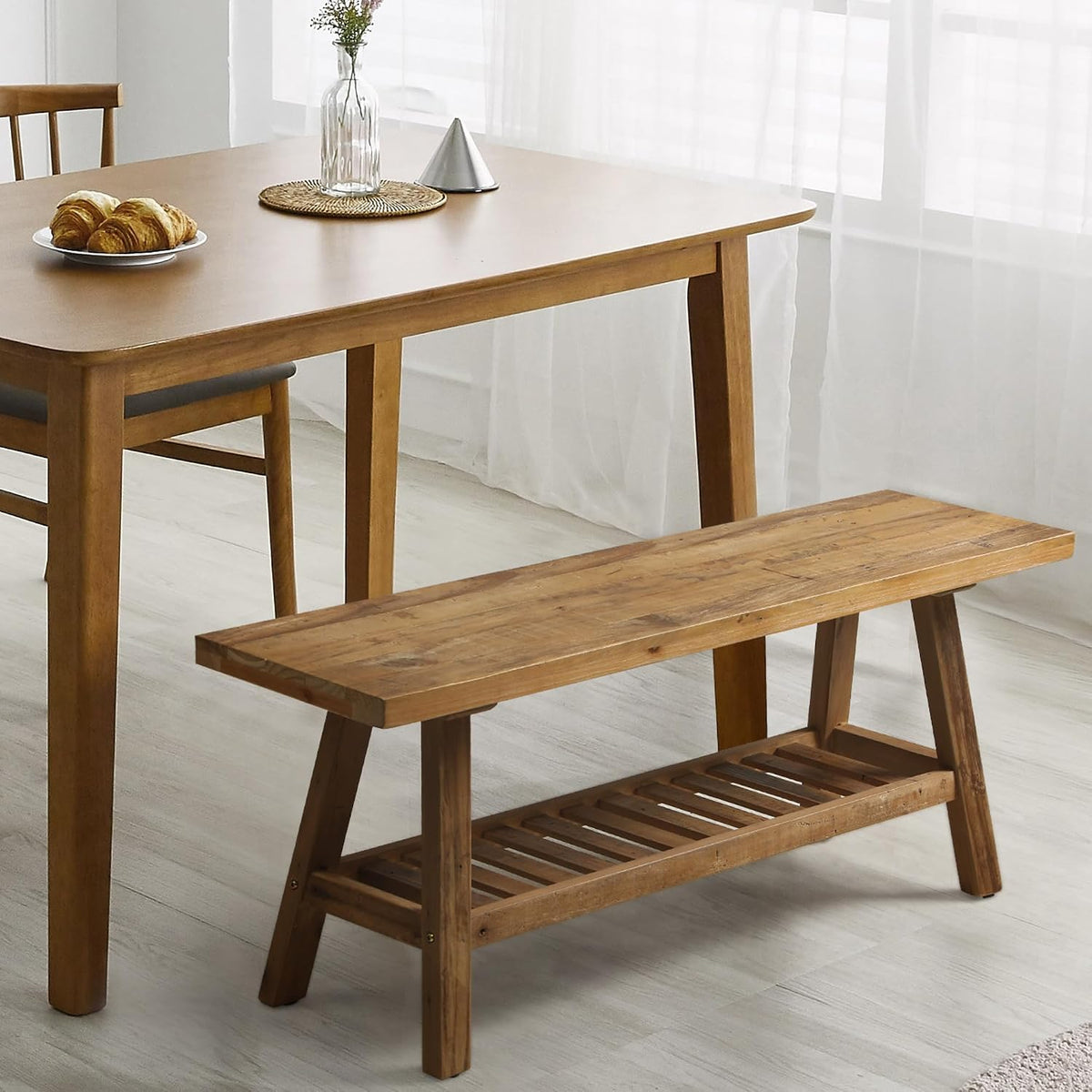 Solid wood bench beside a dining table in a bright room, angled side view showing the lower shelf