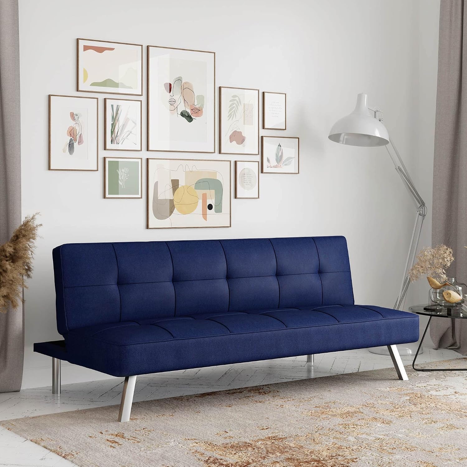 Tufted deep navy convertible futon sofa with chrome angled legs in a styled living room.