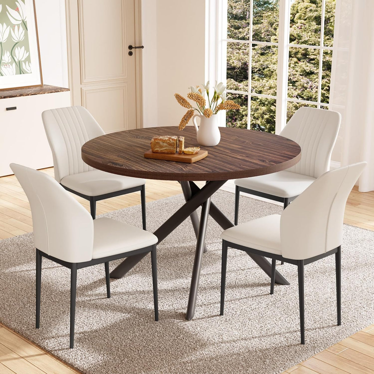 Round dark-walnut tabletop with four white upholstered chairs around it in a sunlit dining area.