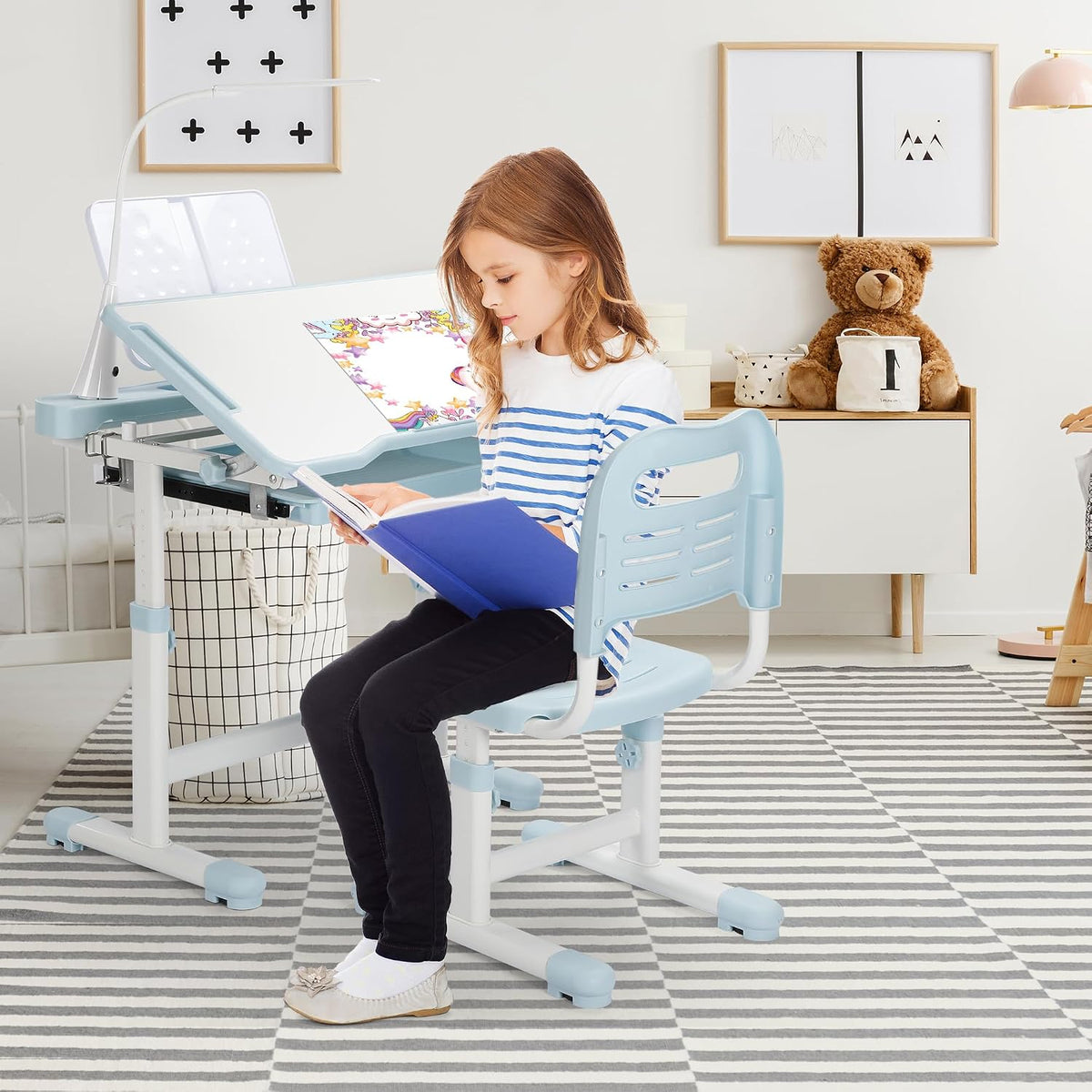 Girl sitting at the height-adjustable blue desk and chair in a bright bedroom with a teddy on a dresser