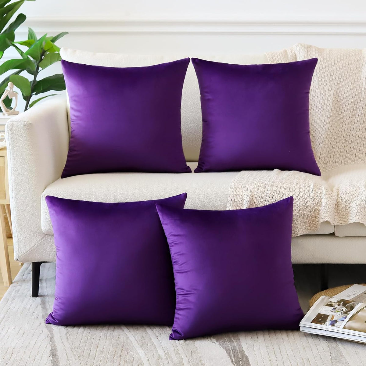 Four square velvet pillow covers in vivid purple displayed on a cream sofa with a throw