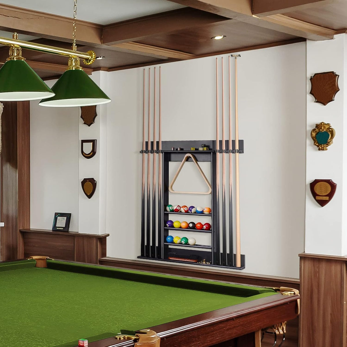 Black wall cue rack with triangle rack and shelves of billiard balls, flanked by cues beside a green pool table.