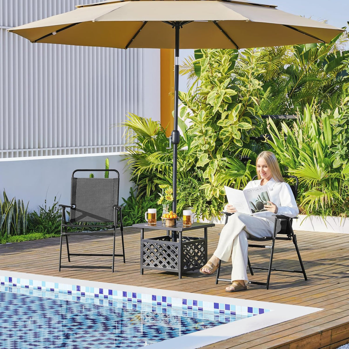 Black Texteline folding patio chairs on poolside deck, lifestyle view with seated woman and umbrella