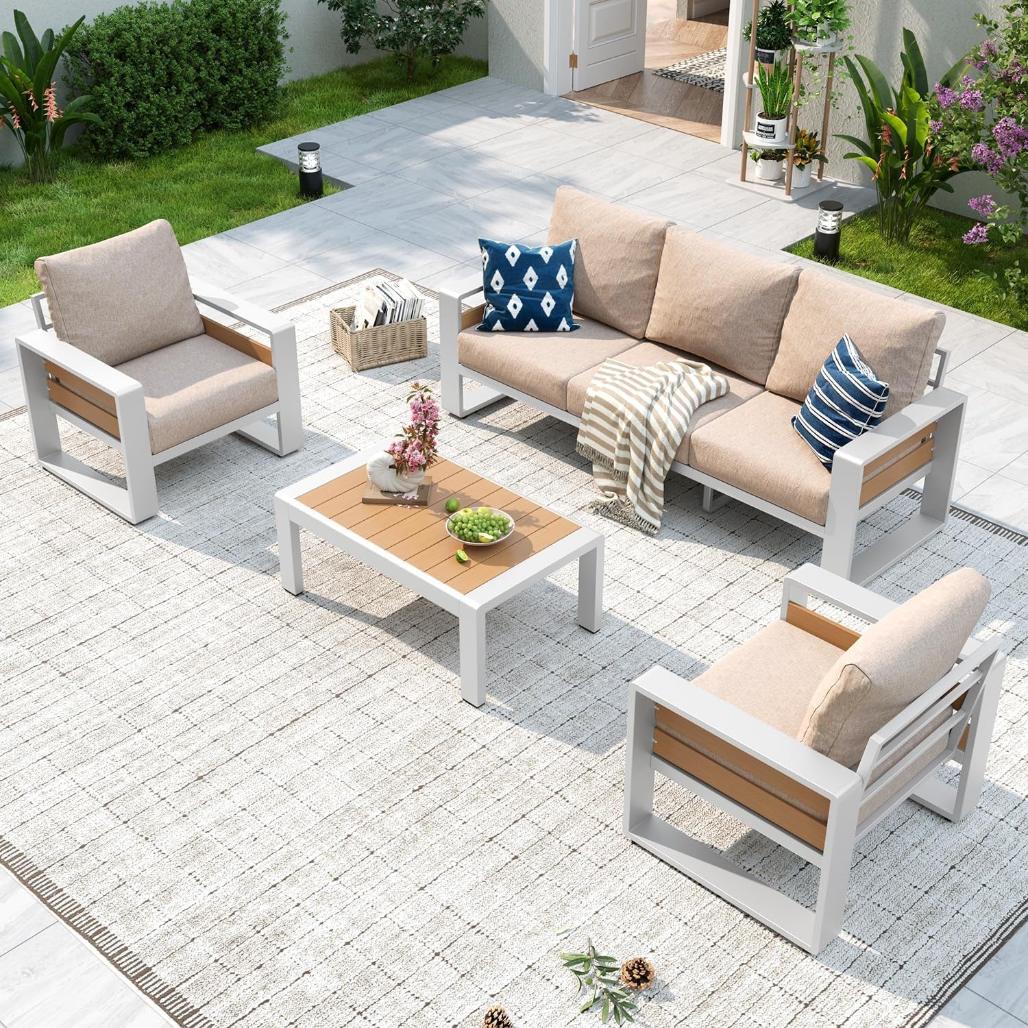 Outdoor patio set in a garden: white-framed sofa and chairs with beige cushions around a wood-top coffee table.