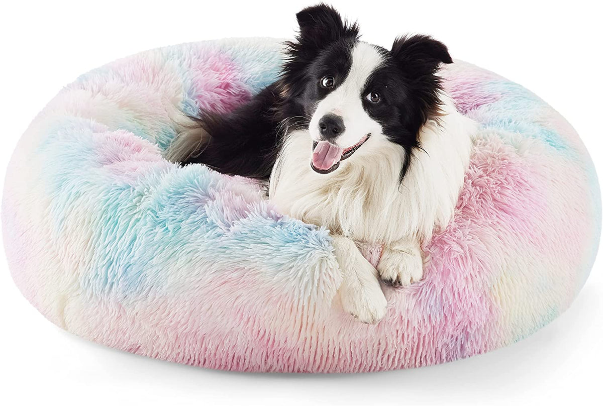 Front view of a pastel multicolor (pink/blue) round faux-fur donut pet bed with a black-and-white dog inside.