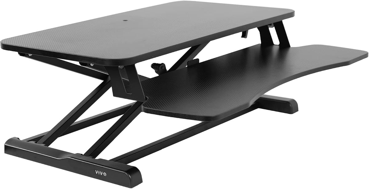 Side-angle close view of a black standing desk converter showing top surface, keyboard shelf and metal scissor frame.