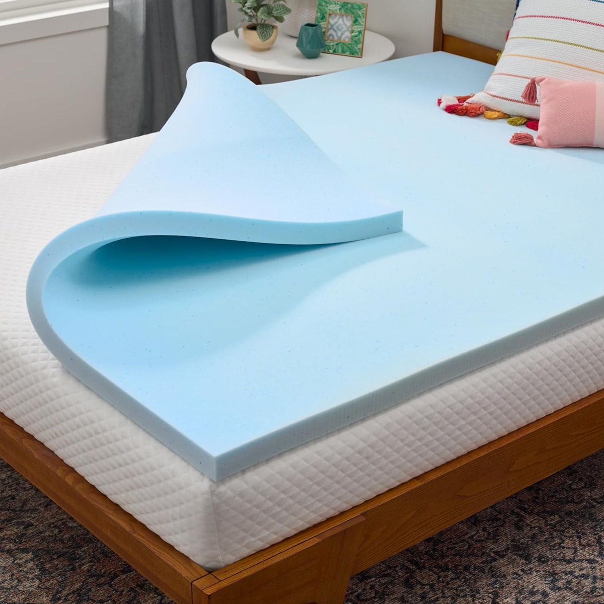 Close-up angled view of a light-blue memory foam topper curled at the corner on a white mattress.