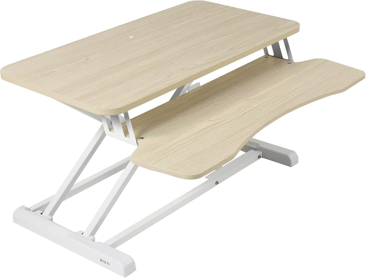 Angled view of a light oak–finish standing desk converter with white metal base and curved keyboard tray