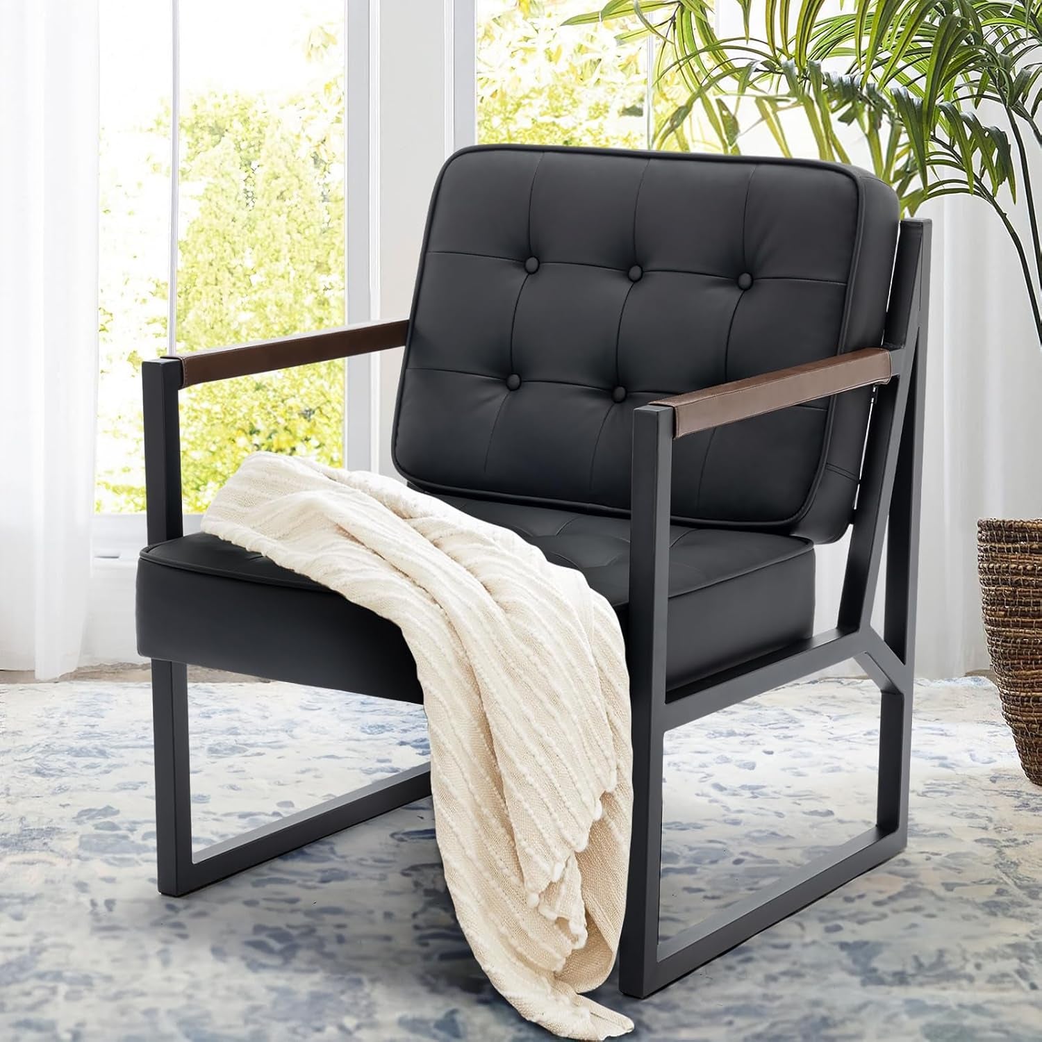 Close-up of a single black tufted chair with metal frame and wooden arm caps draped with a cream throw