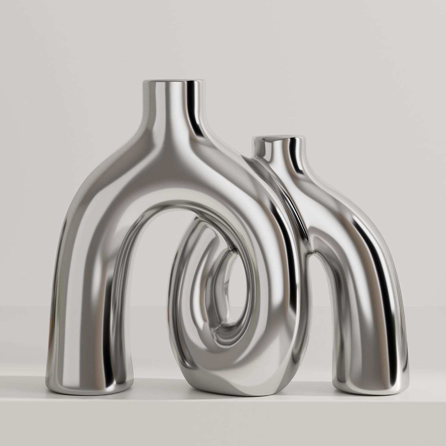 Pair of reflective silver double-arch donut vases photographed against a neutral gray background