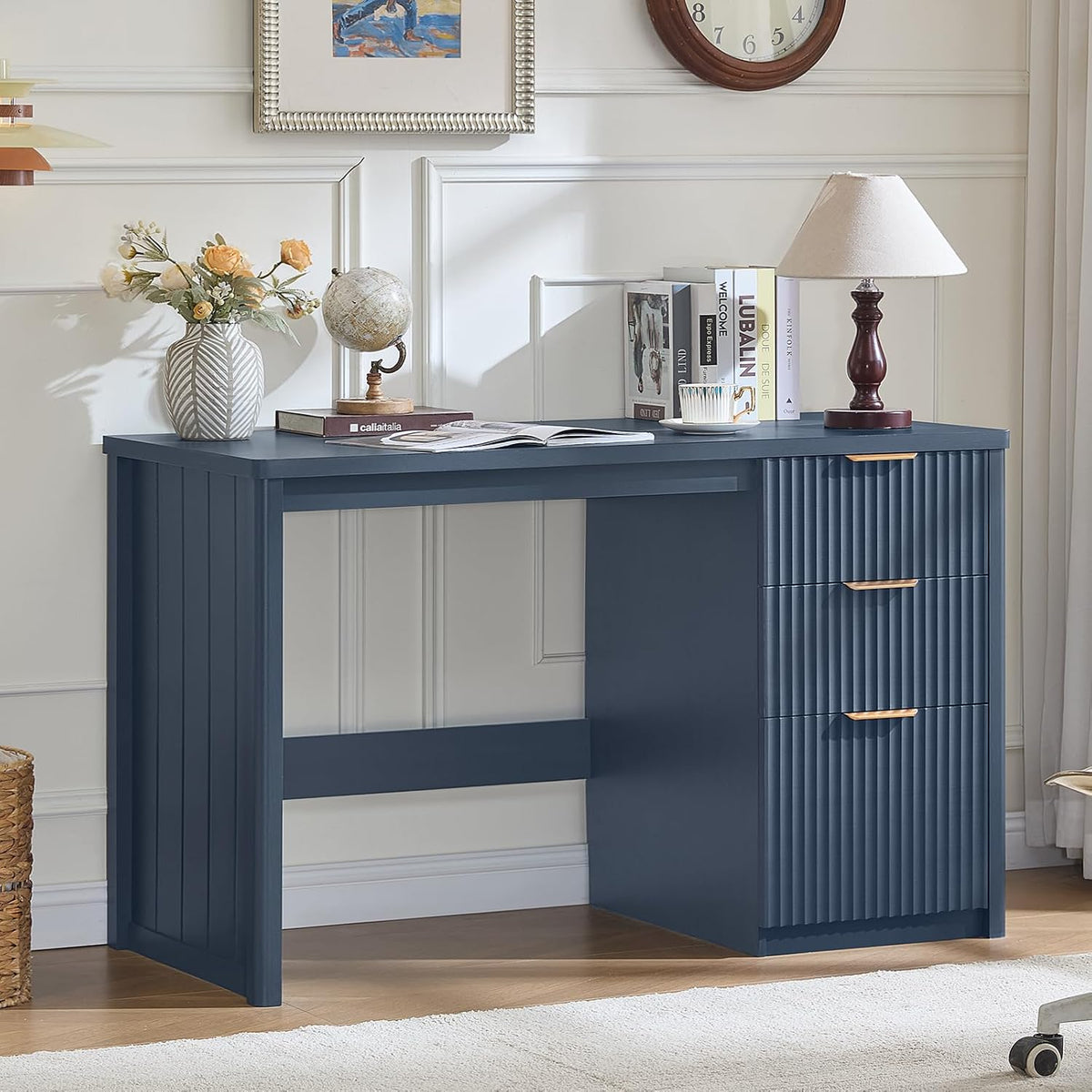 Navy blue fluted desk front-right view styled with books and a lamp against a paneled wall
