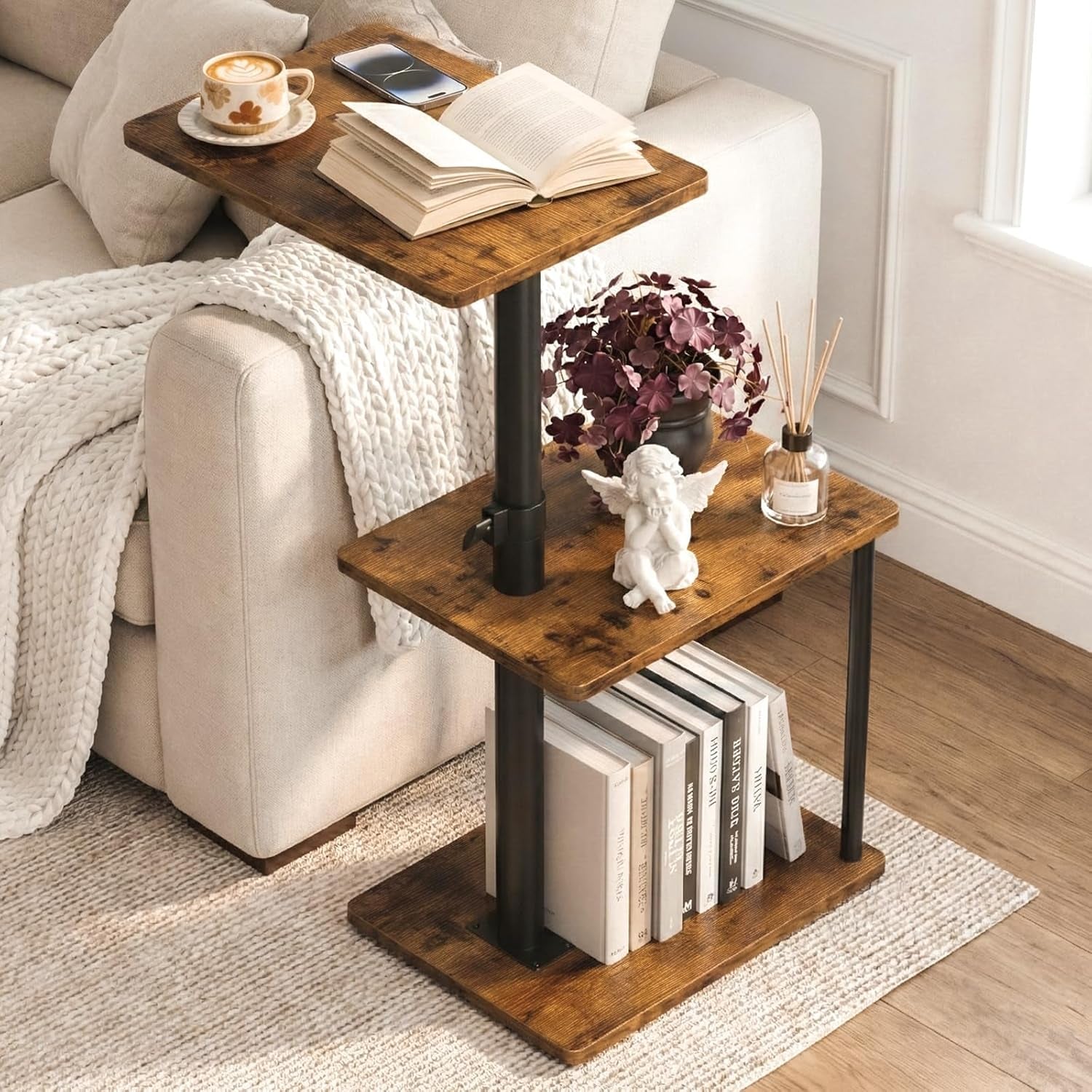 Rustic brown three-tier C-shaped side table next to a cream sofa, angled front view showing books on lower shelf