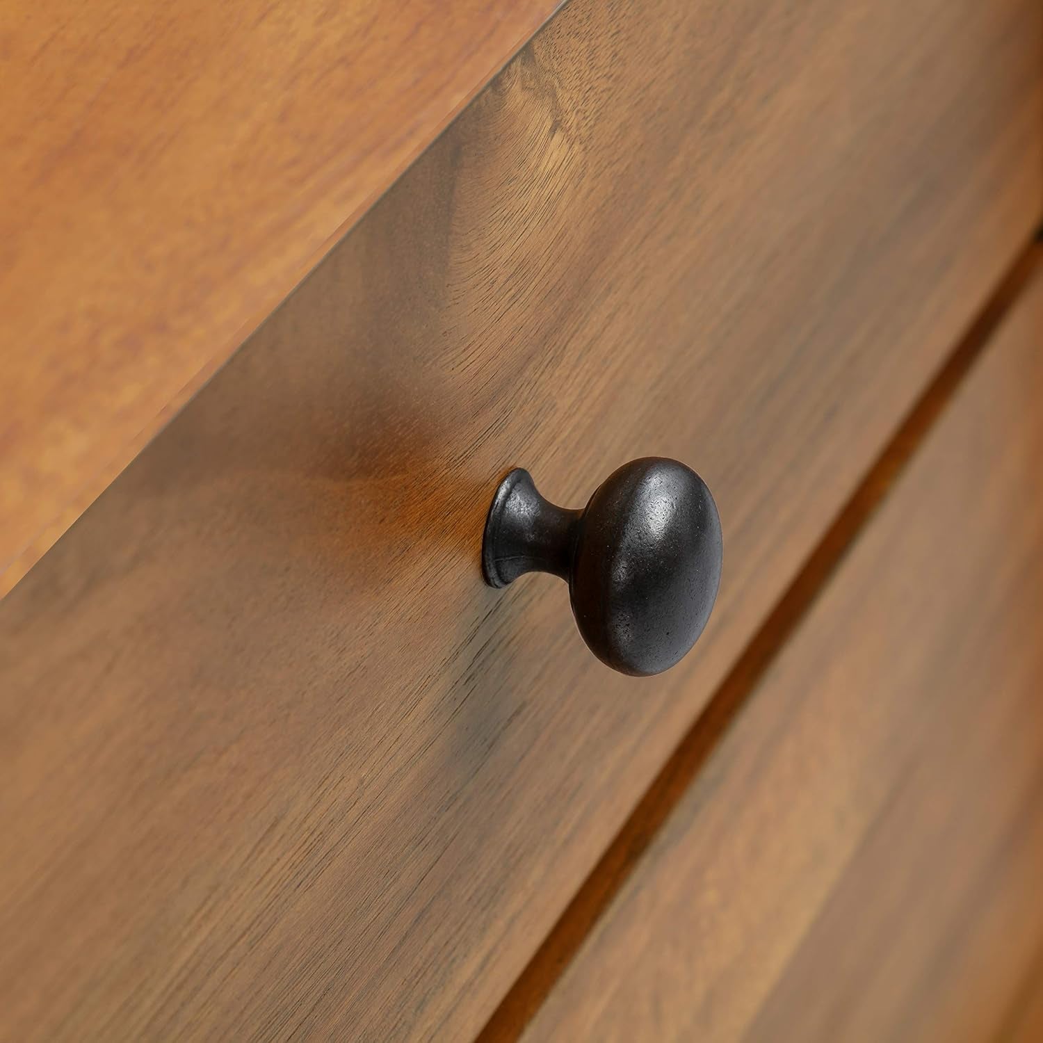 Close-up of a rounded dark metal drawer knob on warm wood veneer.