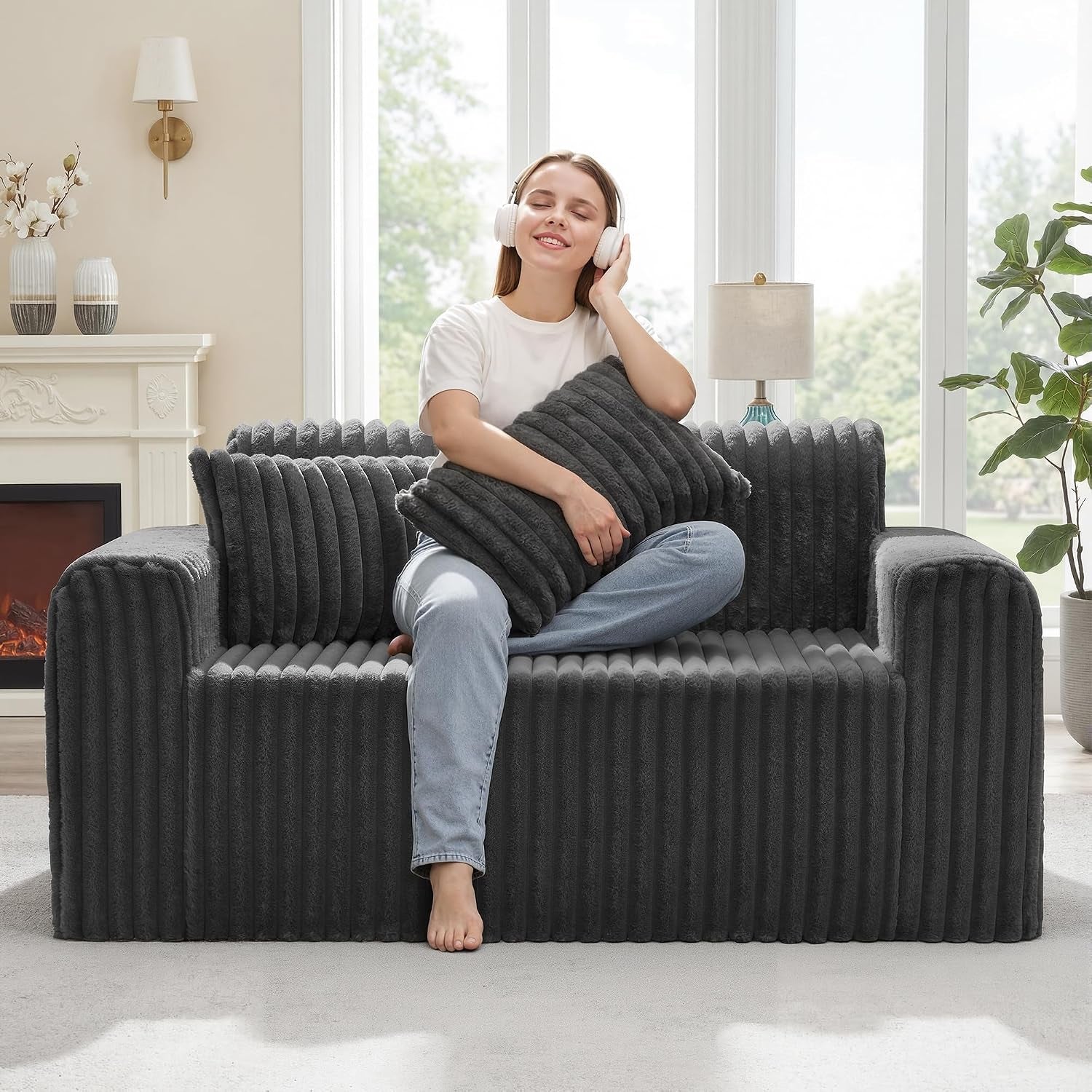 Dark gray ribbed floor sofa in a sunlit room with a woman seated cross‑legged hugging a matching cushion.