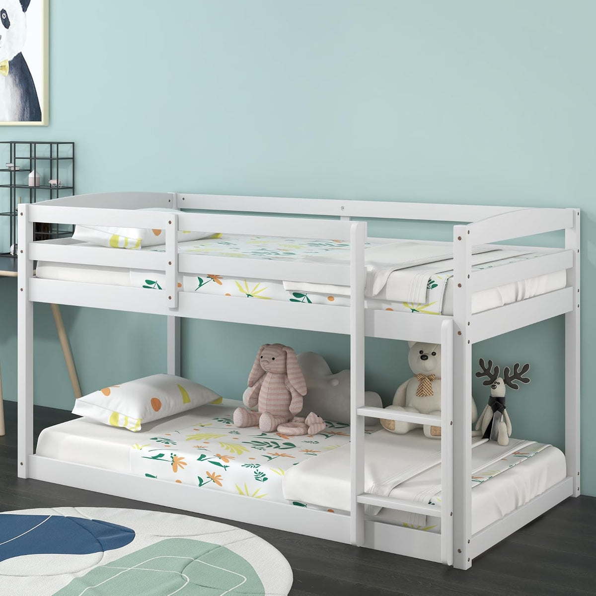 Side view of the white low bunk bed against a teal wall, fitted with floral bedding and stuffed toys below.