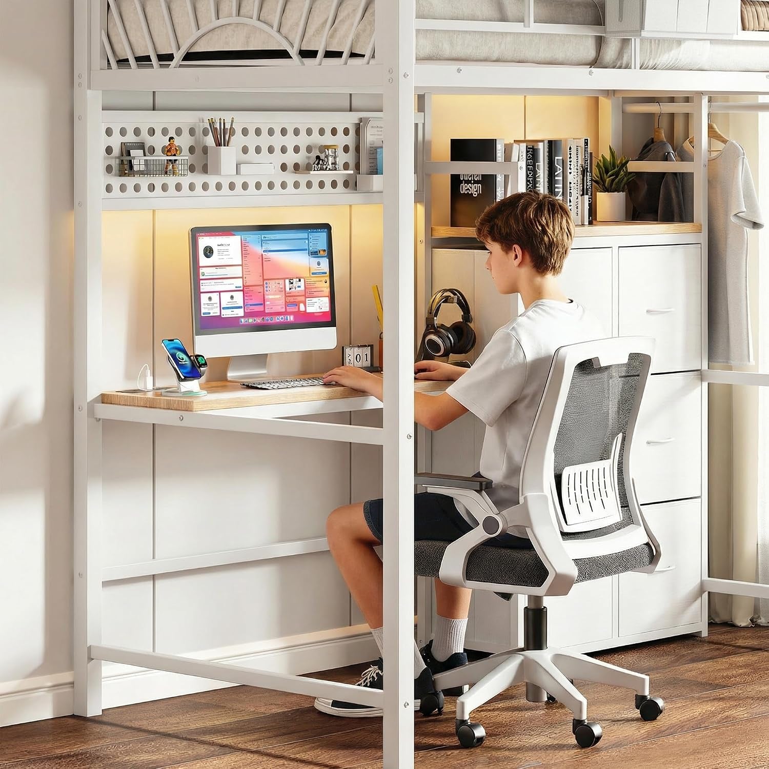 A boy seated at the desk under the loft bed using a computer, with a rolling office chair and shelving above the workspace.