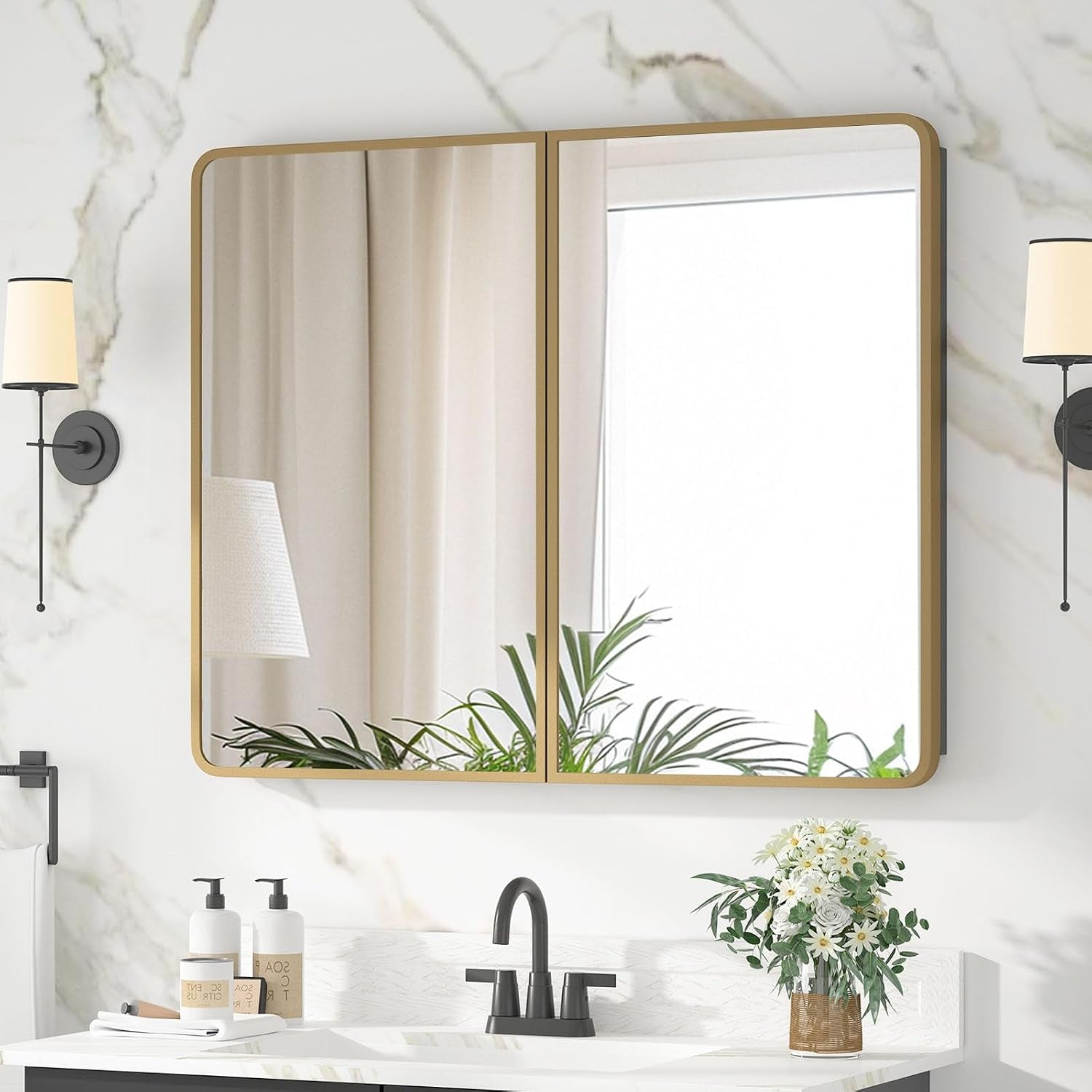 Wall-mounted double-door mirrored medicine cabinet with gold frame above a sink and wall sconces.