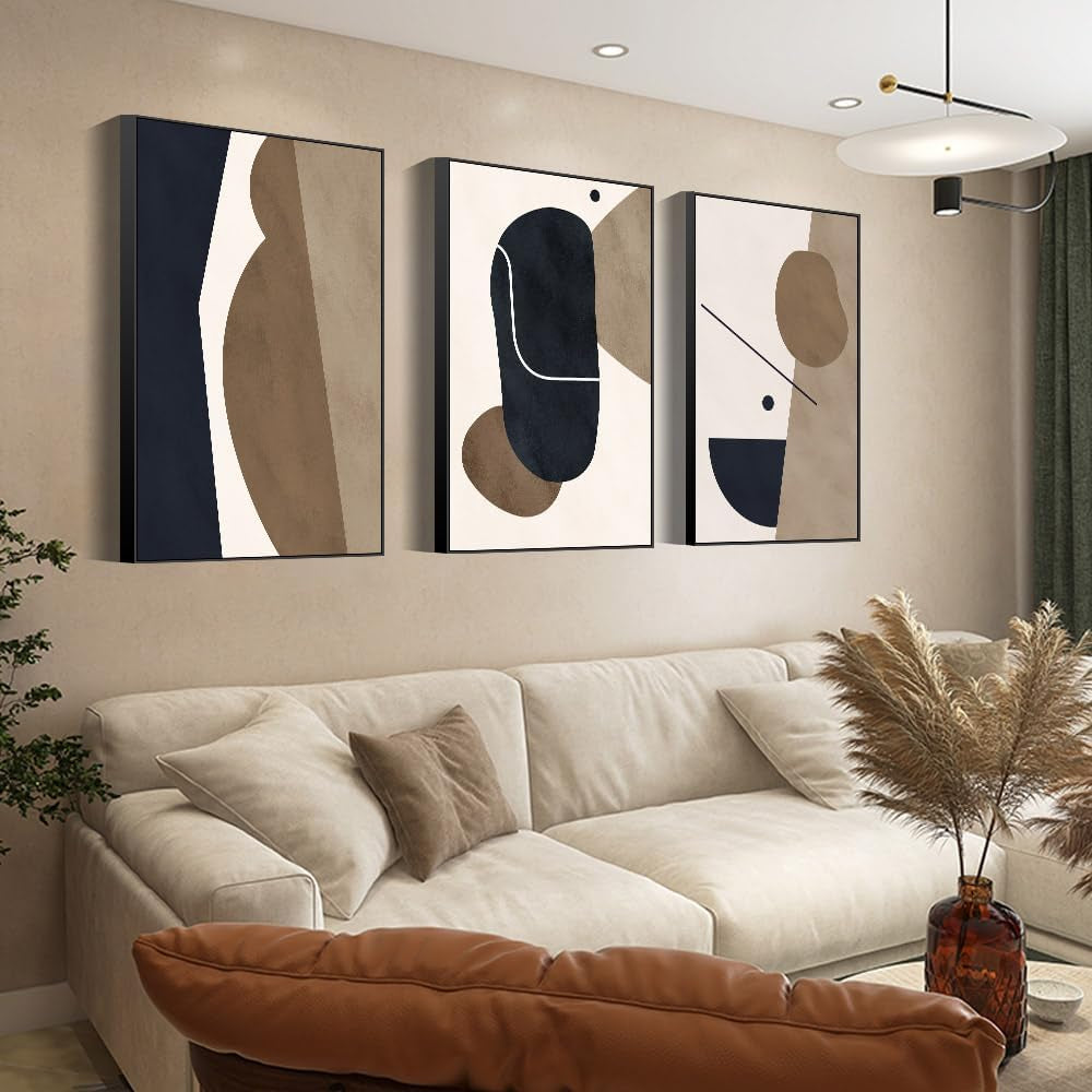 Angled side view showing the canvas frames' depth and shadow as three abstract pieces hang over a sofa beneath recessed