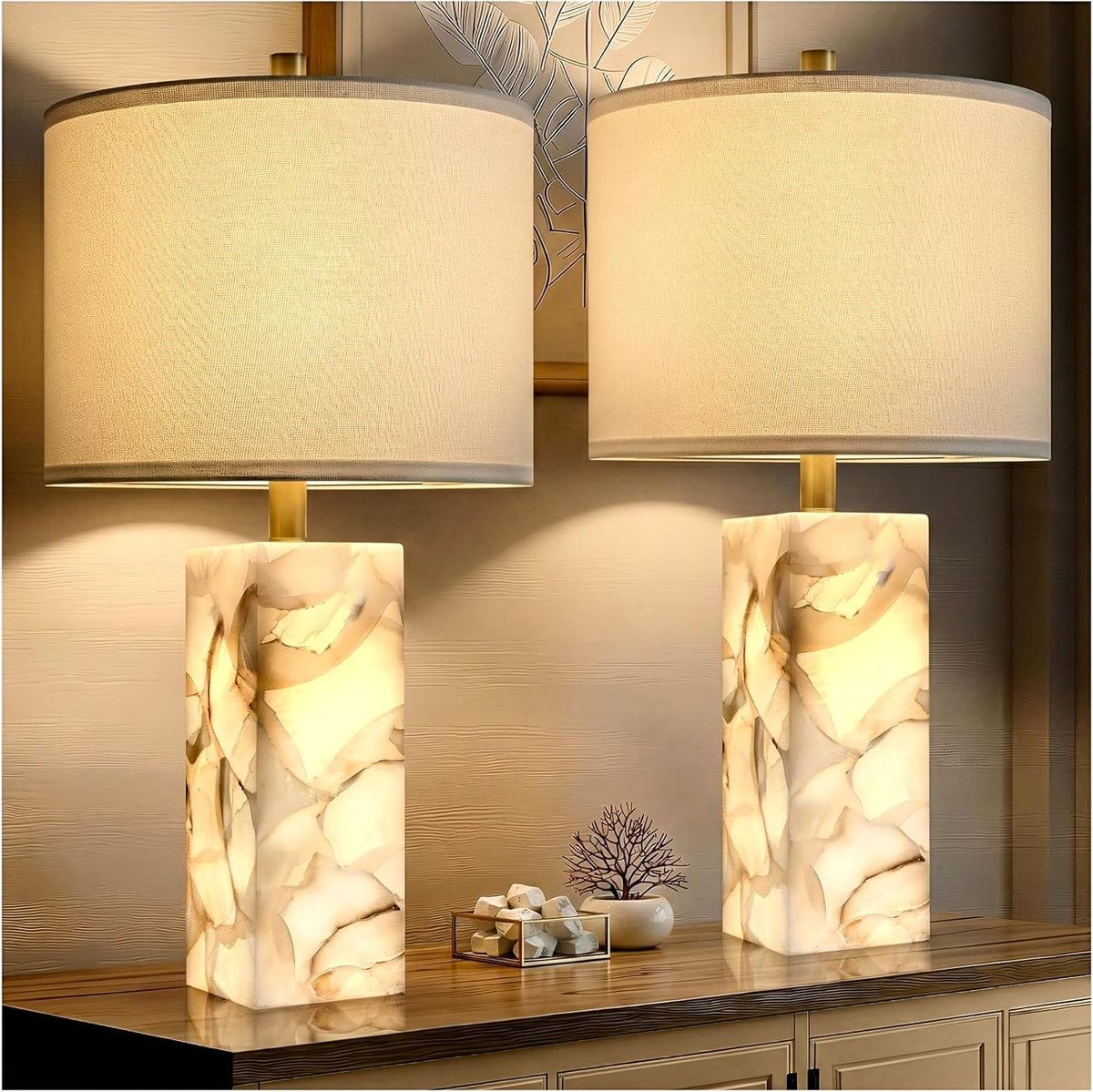 Two illuminated alabaster column table lamps with white linen shades on a wooden console table