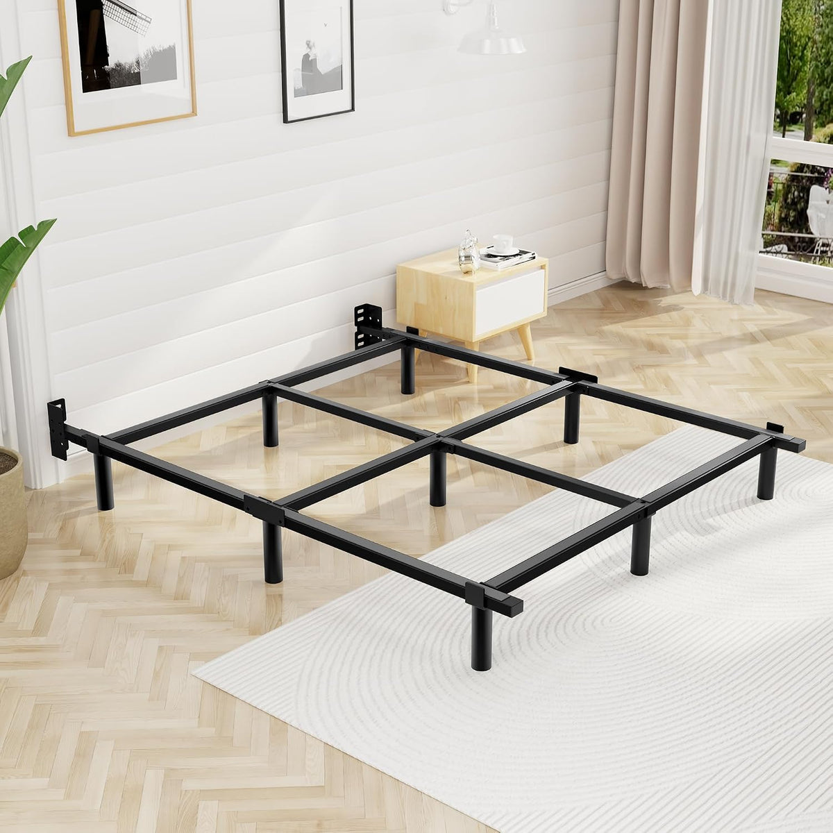 Empty black steel bed frame assembled on herringbone floor in a bright bedroom.