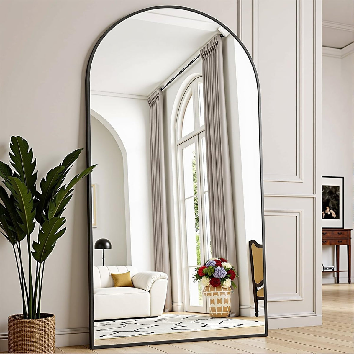 Close-up of an arched full-length mirror edge showing the slim black frame and reflected window drapery.