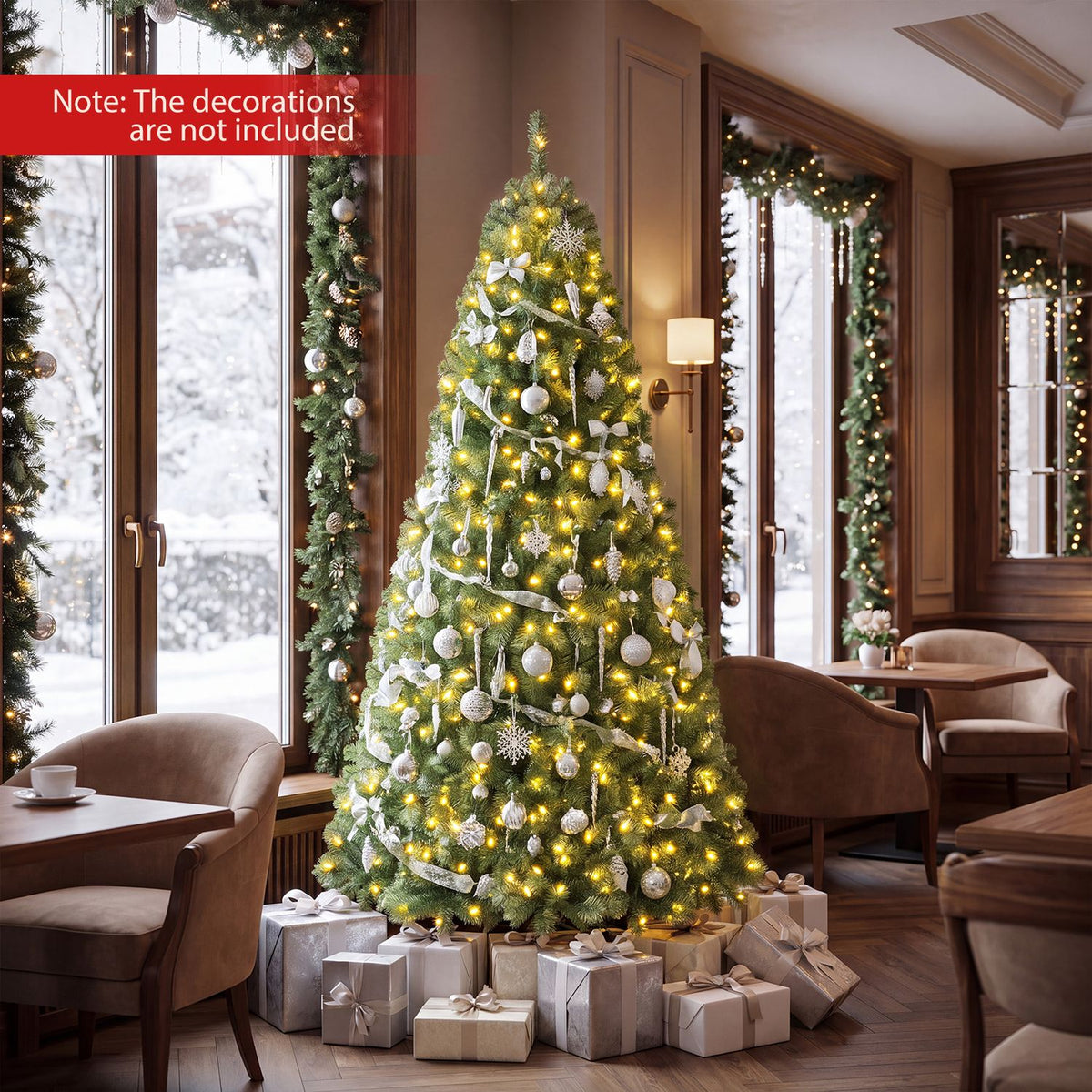 A decorated, glowing Christmas tree stands among dining chairs and wrapped gifts by tall windows.