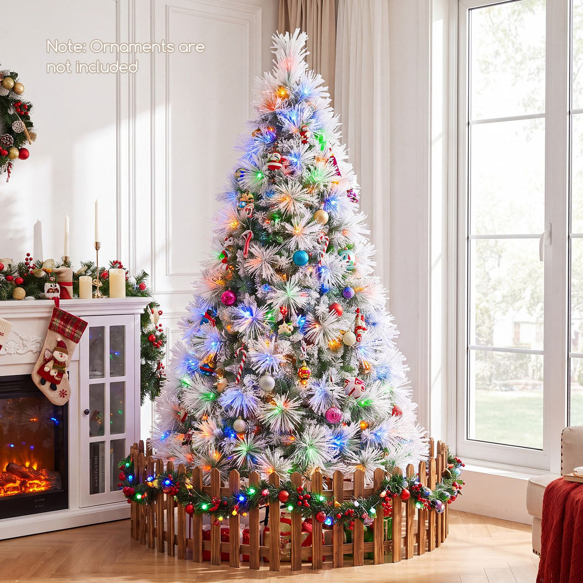 Flocked tree with colorful lights and ornaments beside a fireplace and tall window.