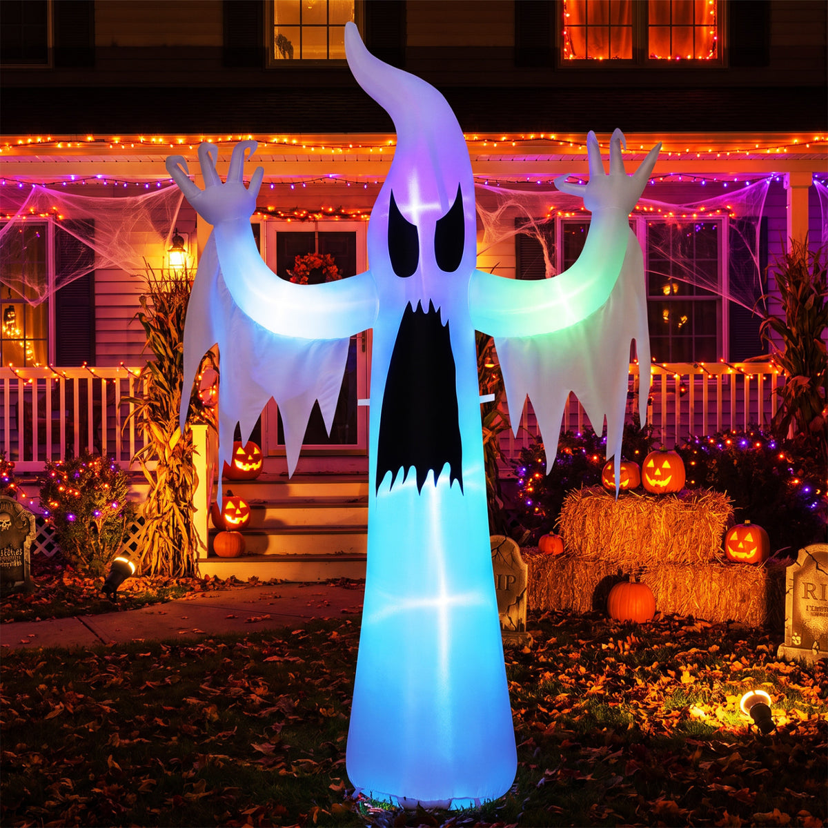 The ghost inflatable glows in blue, green, and purple in front of a Halloween-decorated house.