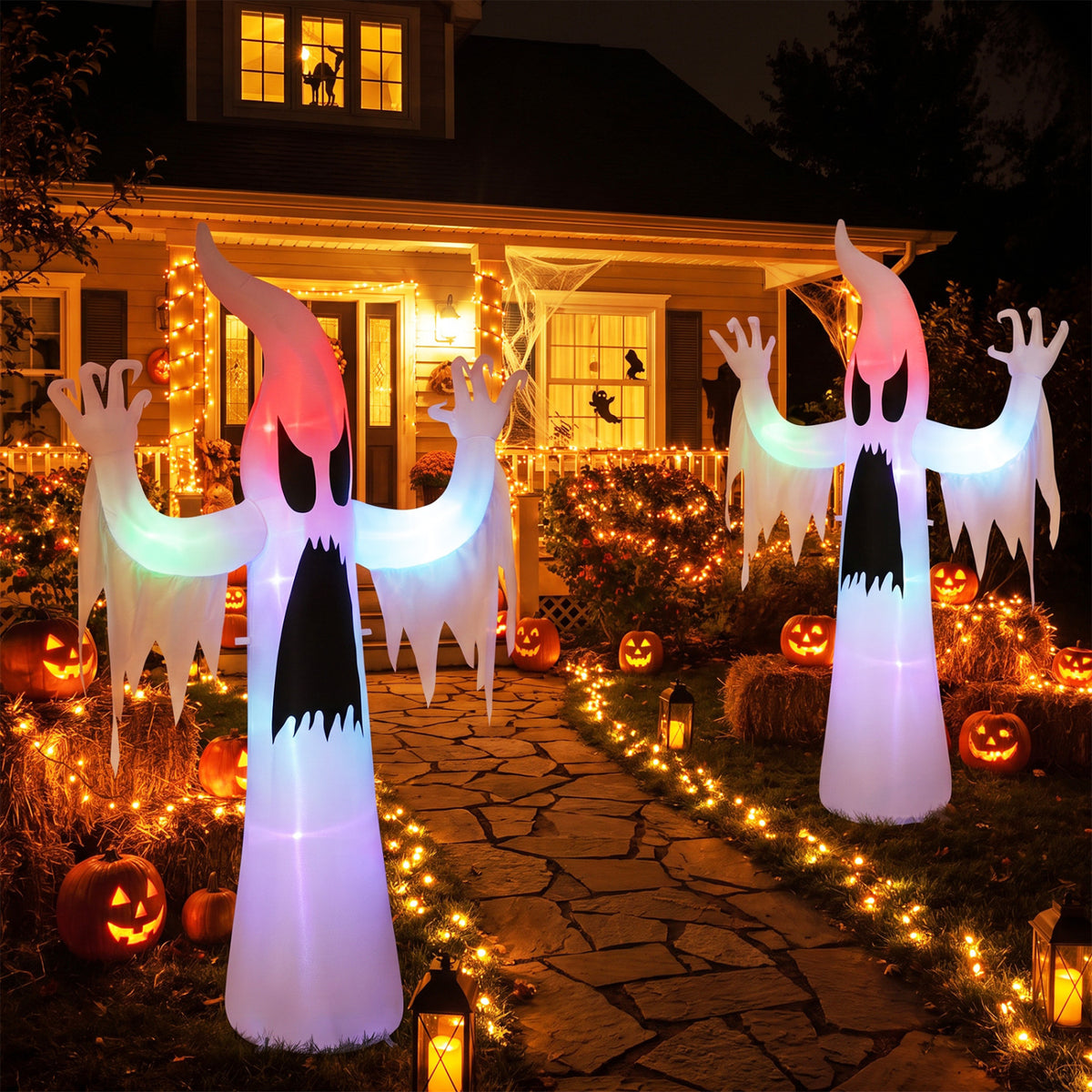 Two glowing ghost inflatables stand along a Halloween-decorated garden path at night.