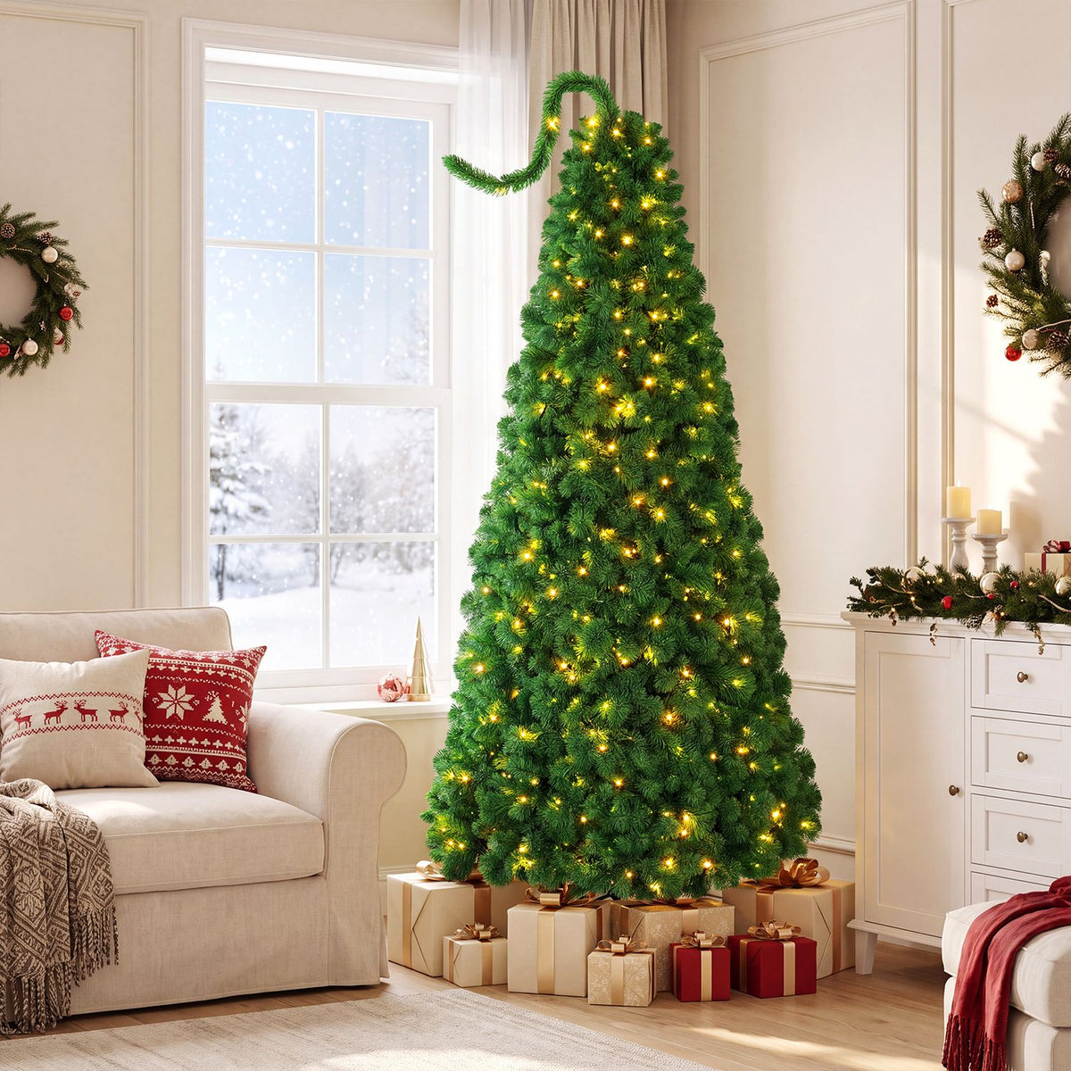 Green flocked Christmas tree glowing with warm lights beside a sofa and snowy window.
