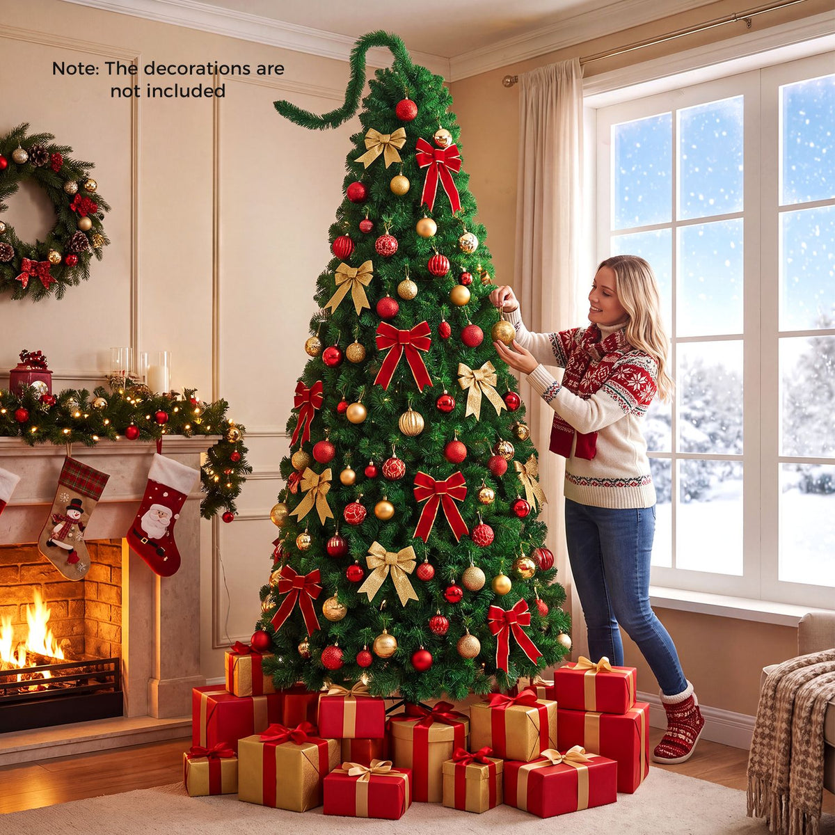 A woman decorates a lit green Christmas tree with red and gold ornaments beside a fireplace.