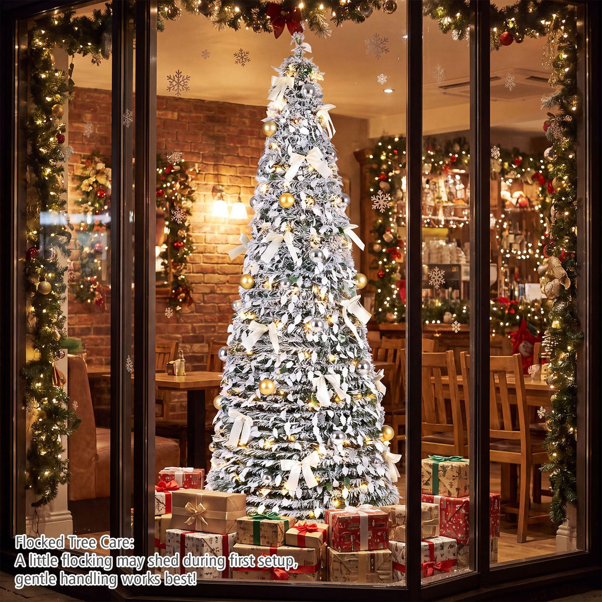 Snow-flocked, warmly lit Christmas tree with gold ornaments and white bows displayed among festive window decorations.