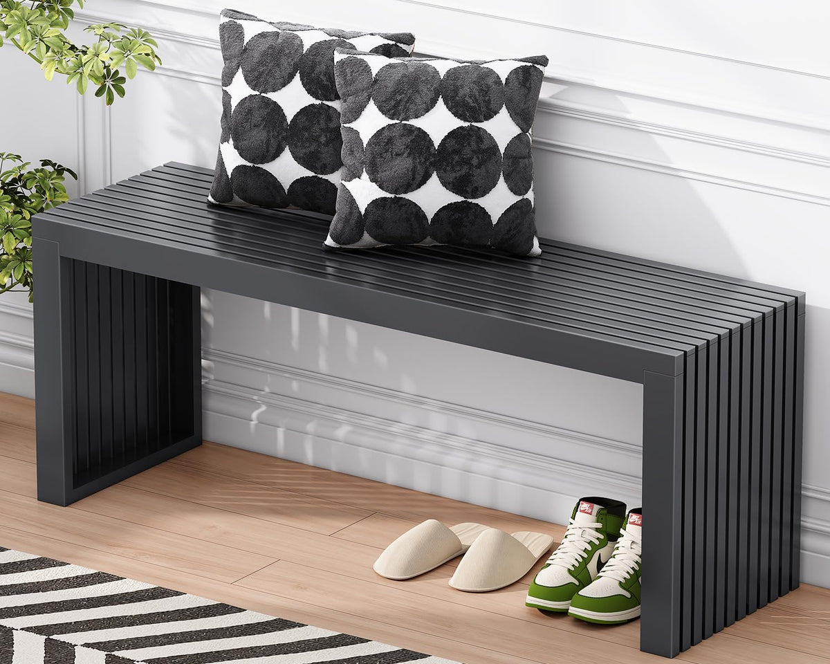 Black slatted bench placed against a white wall, styled with two patterned pillows and shoes underneath.