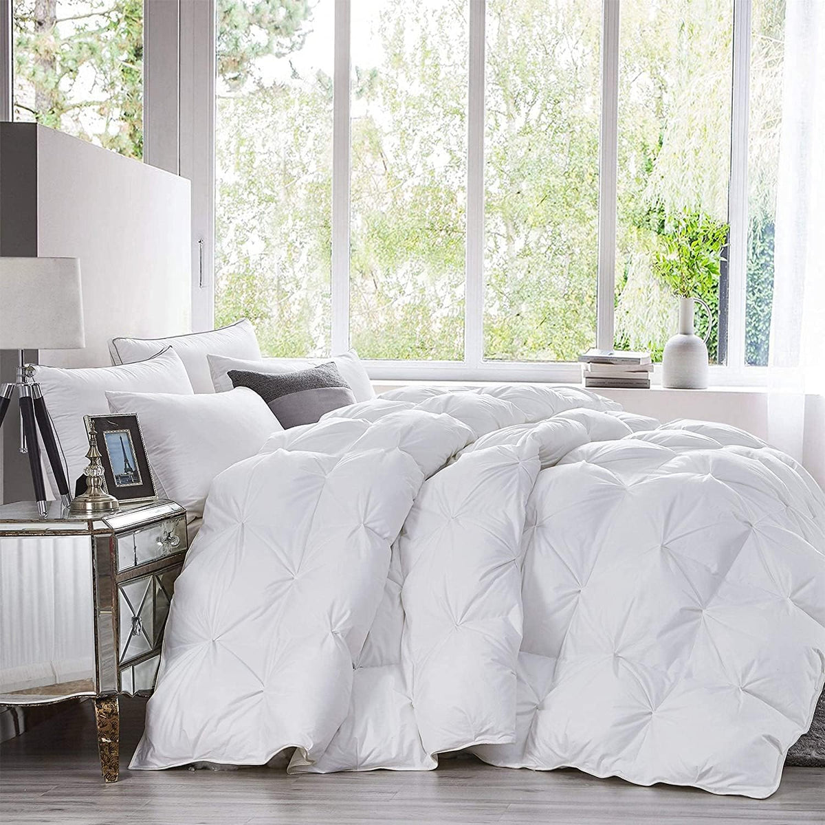 Bright bedroom with a plump white tufted comforter draped over a made bed by a large window.