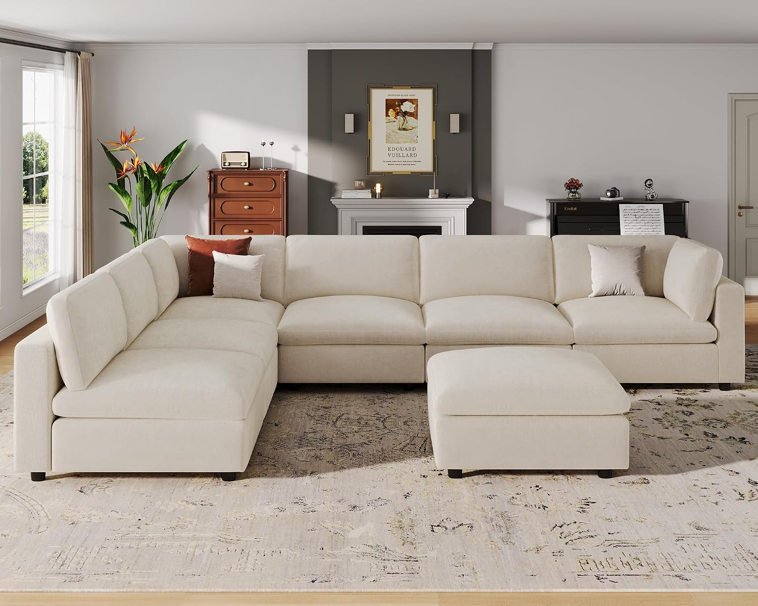 Wide front view of a cream modular corner sectional with a matching movable ottoman on a patterned rug.