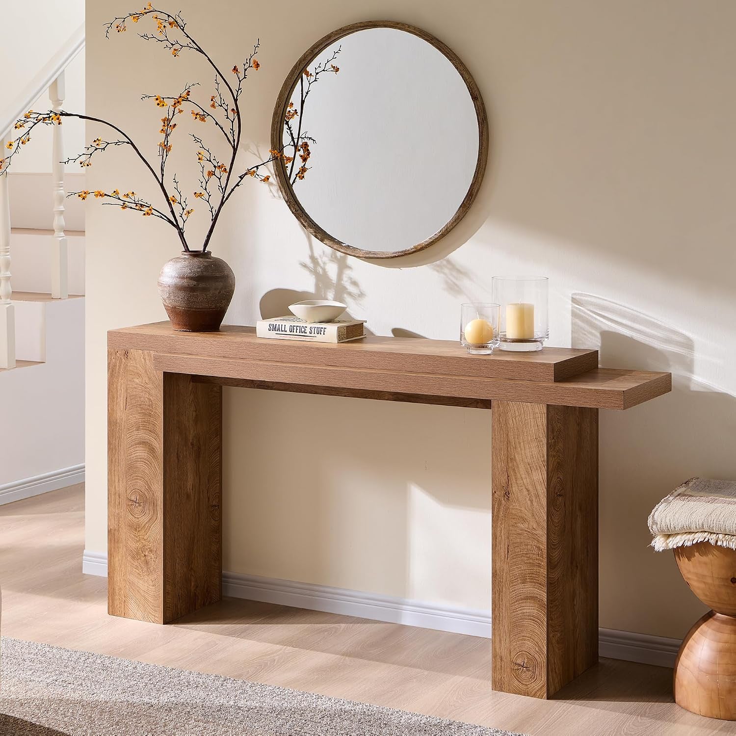 Console table in a light wood finish under a round mirror with a vase, book, and candles on top.