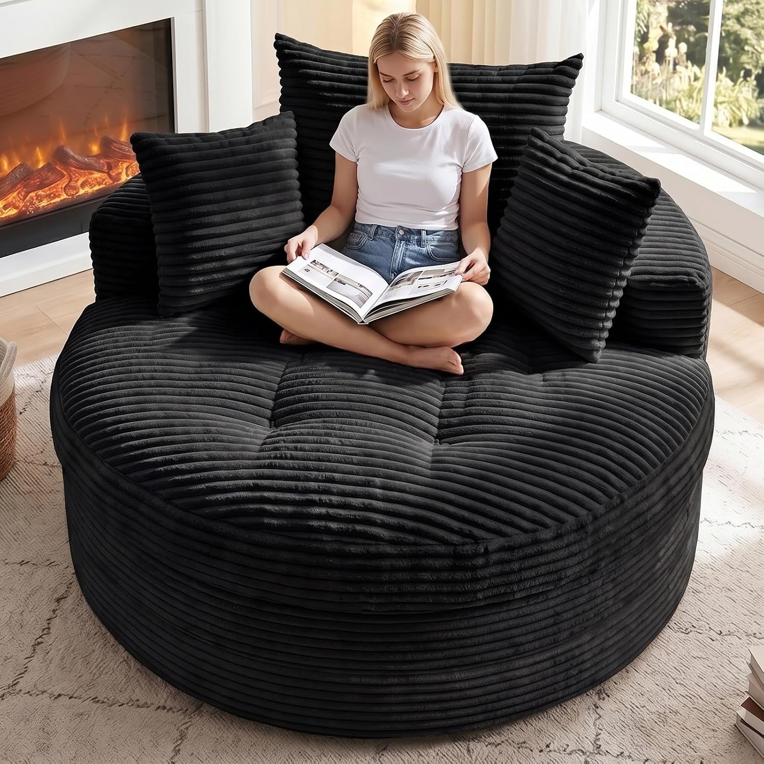 Top-front view of a round black corduroy floor chaise with three matching pillows and a person reading a book.