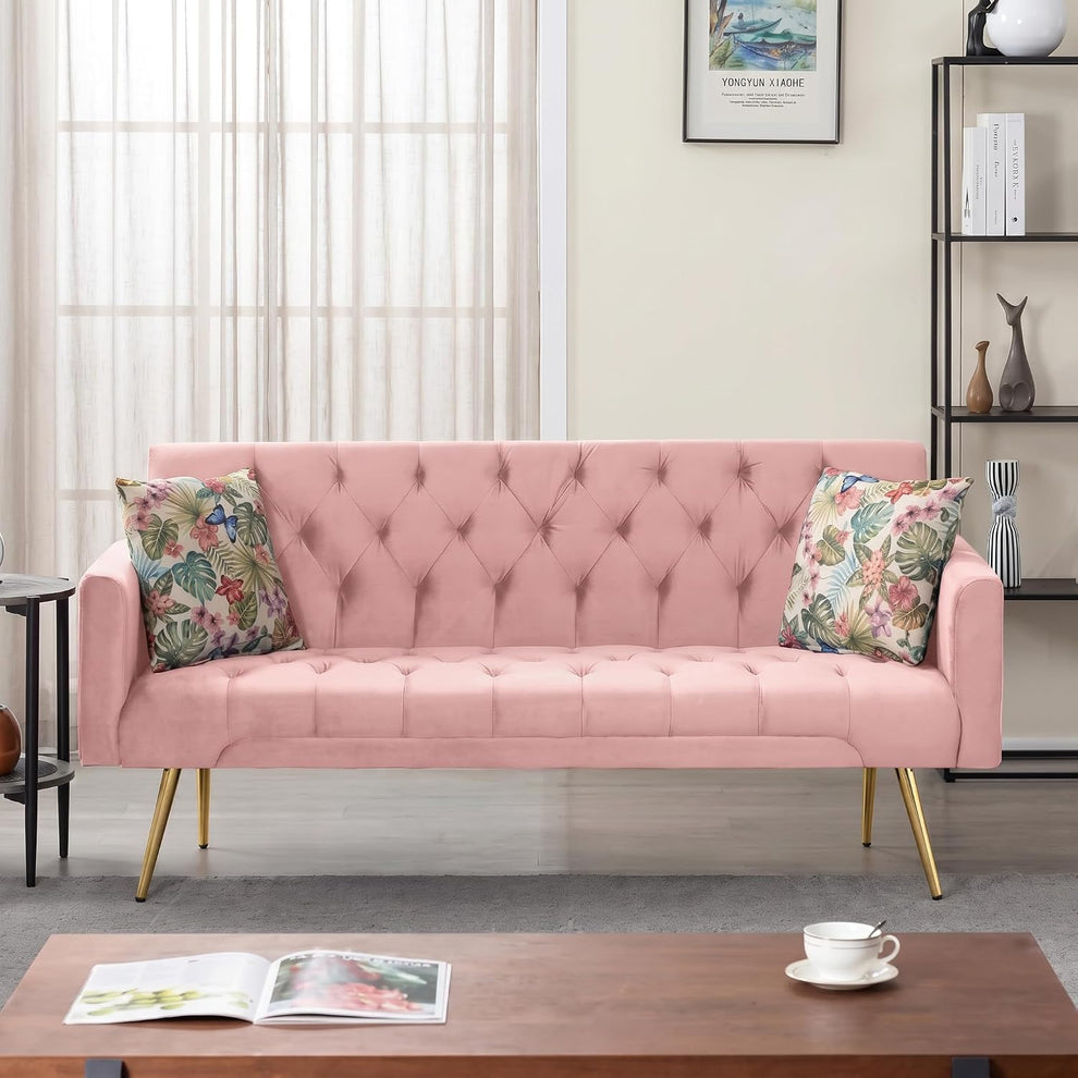 Front view of a pink tufted velvet sofa with floral throw pillows and gold legs in a living room.