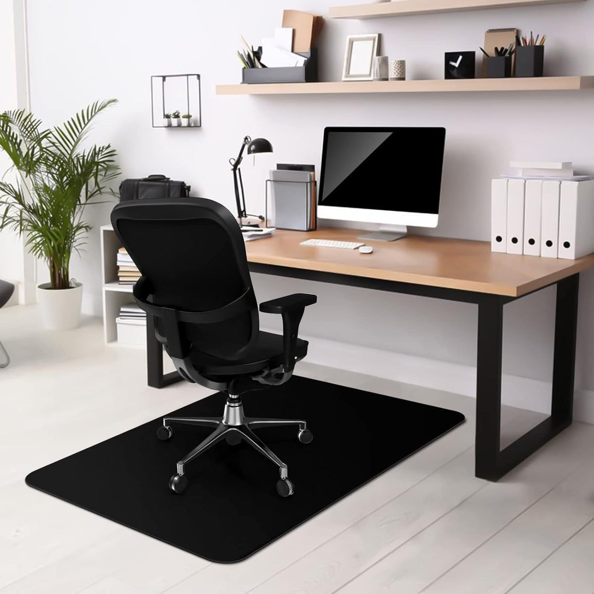 Black rectangular mat option placed beneath a black swivel chair at a wood-topped desk, contrasting with light flooring.