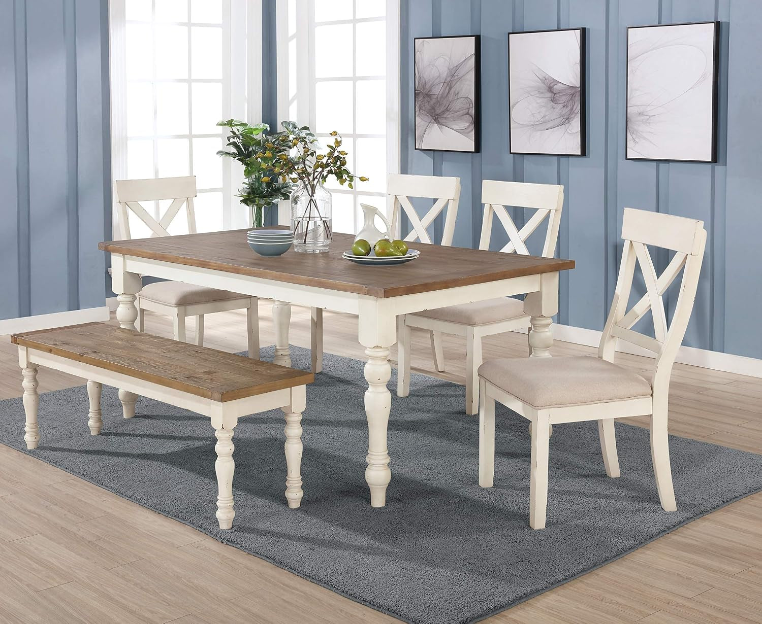 Angled view of the dining table and matching bench with four cross-back upholstered chairs in antique white and distressedoak