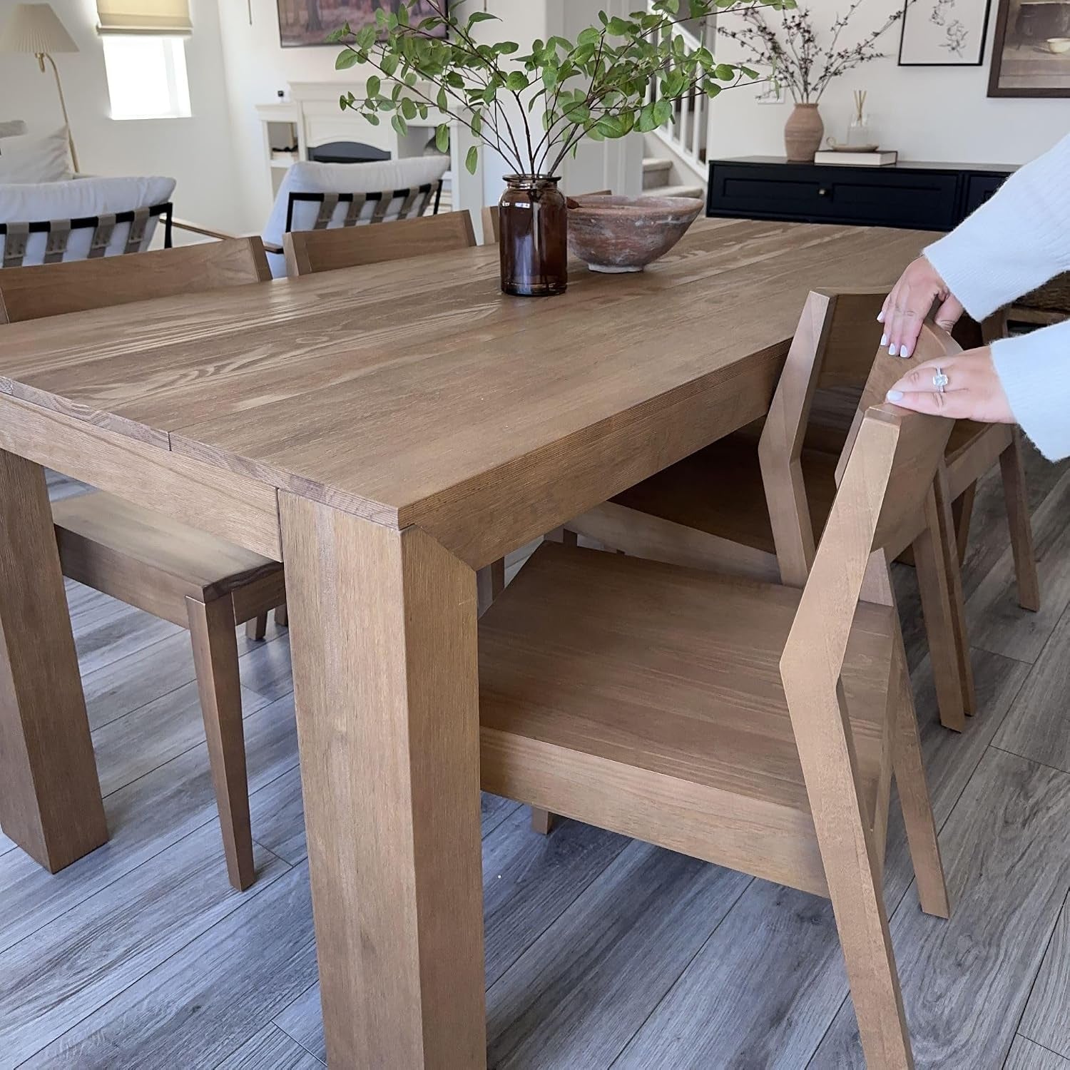 Three-quarter view of the dining table with matching bench and a person pulling out a wooden chair.
