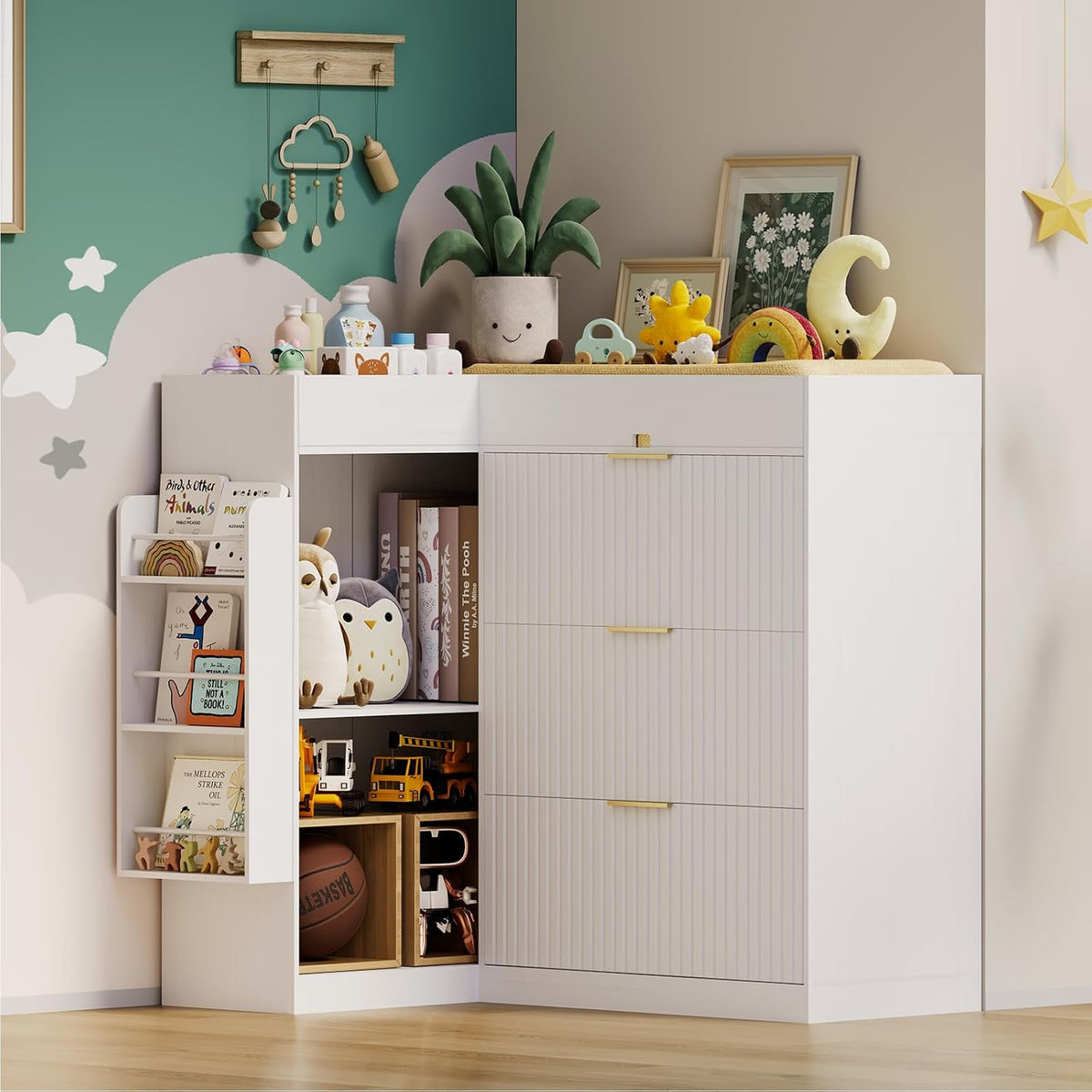 Corner view of a white changing dresser with vertical grooved drawer fronts, gold handles, and a slim side book rack filled