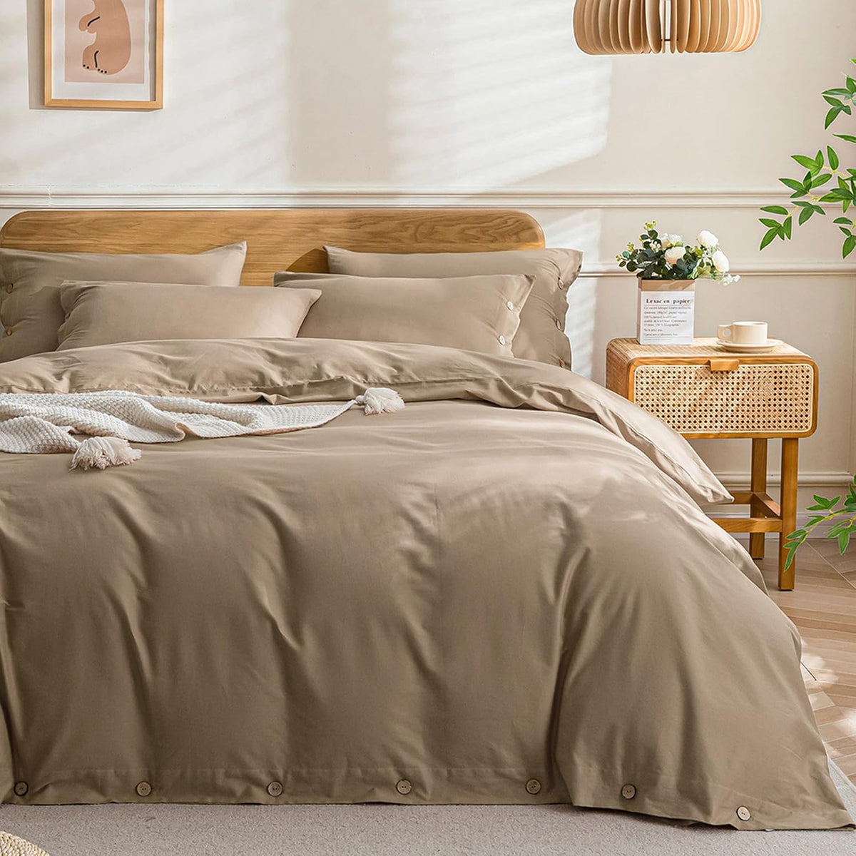 Front view of a made bed with warm tan washed-cotton duvet showing wooden button closures, tassel throw and cane nightstand