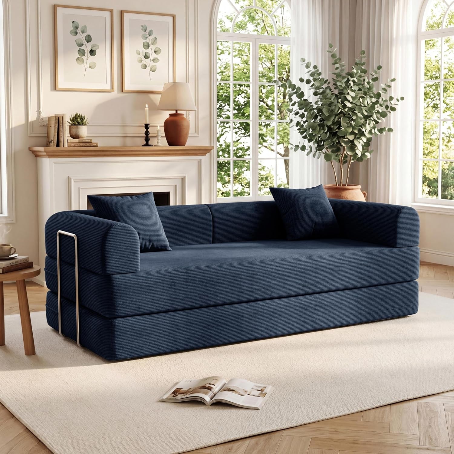 Navy corduroy convertible sofa bed in a sunlit living room with pillows and fireplace behind