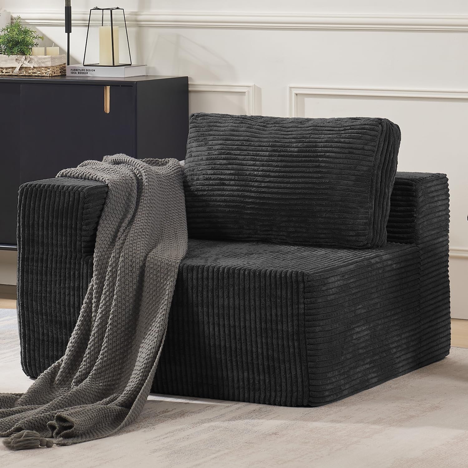 Three-quarter view of a single modular sofa seat with arm, in deep charcoal ribbed fabric and a textured gray throw.