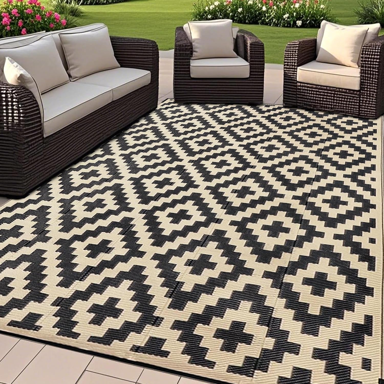 Patio seating arrangement with dark woven sofa and chairs placed around a black-and-cream geometric outdoor rug.
